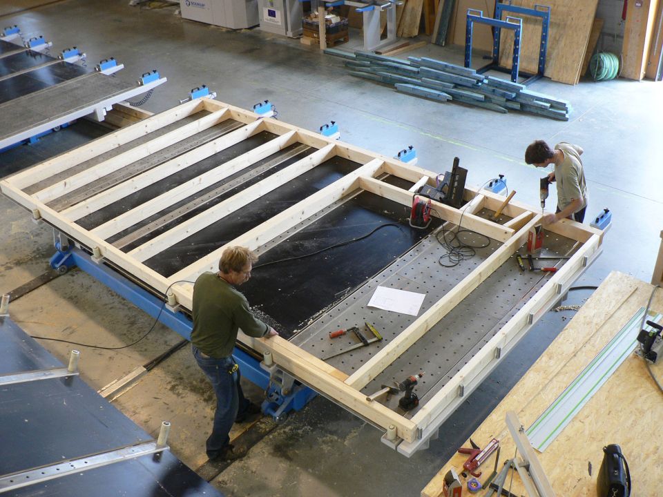A person measuring timber planks with a metal ruler and pencil on a workshop bench